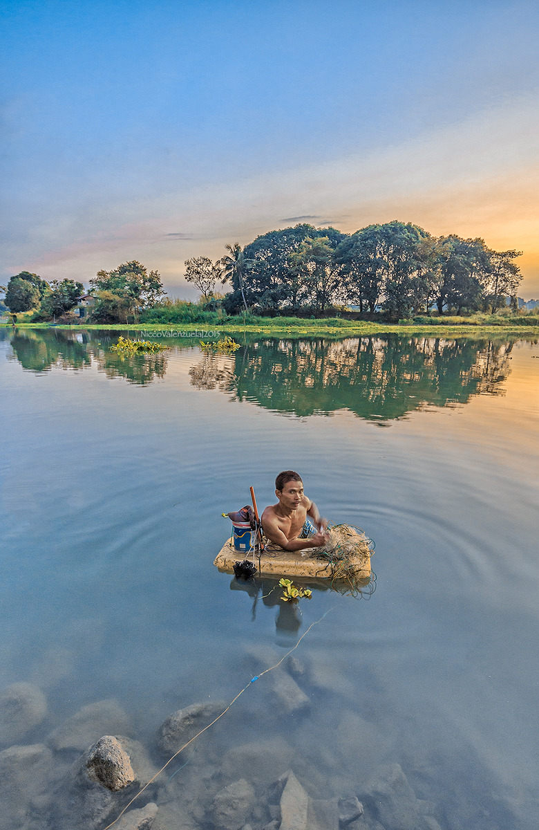 A man using an improvised floating device to harvest the fish in his nets. 

Angat River, Pulilan, Bulacan, Philippines January 2015